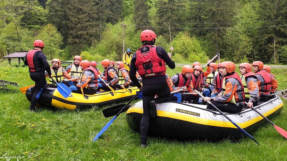 A group of people in inflatable rafts wearing life jackets and helmets, paddling on a grassy riverbank. 4