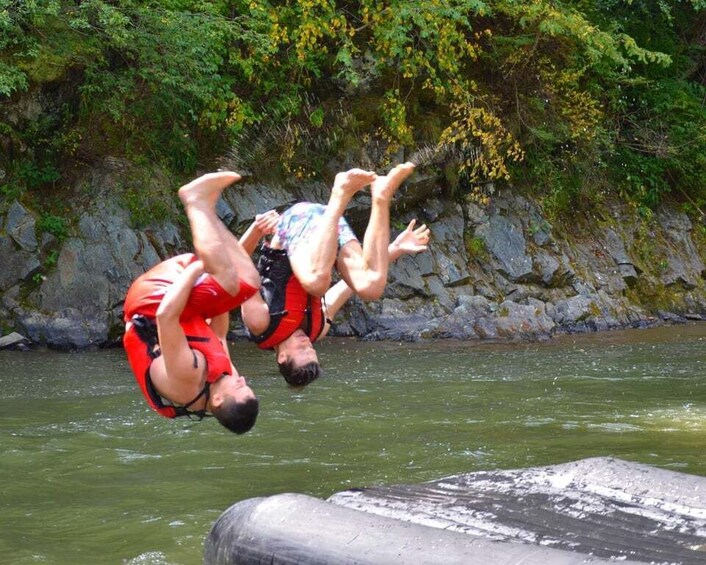 Two people in red life vests jumping off a concrete structure into a river. 5