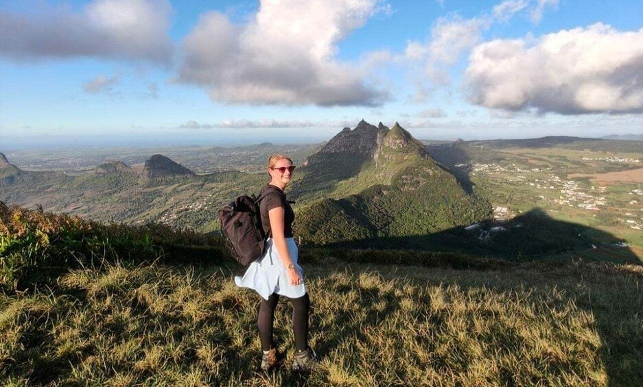 A person standing on a grassy hill overlooking a mountainous landscape with a town in the valley below. 1