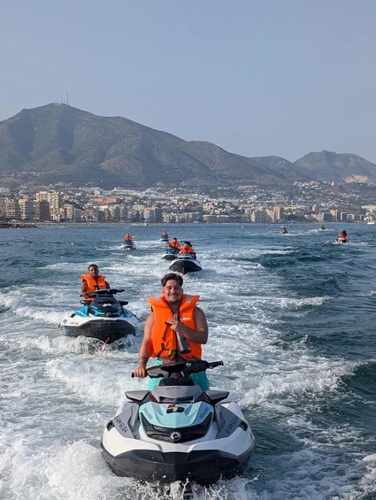 A person riding a jet ski on a body of water with a cityscape and mountains in the background. 1