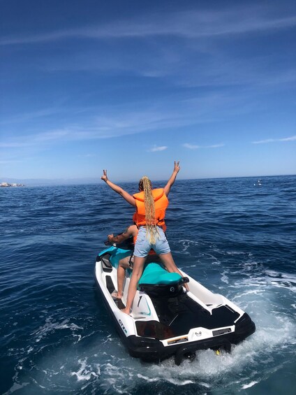 A person on a jet ski with arms raised, another person seated, and a third person standing behind. 2