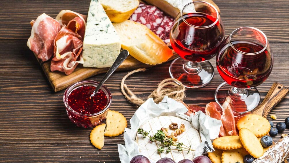 A charcuterie board with various meats, cheeses, and crackers, accompanied by glasses of red wine. 5