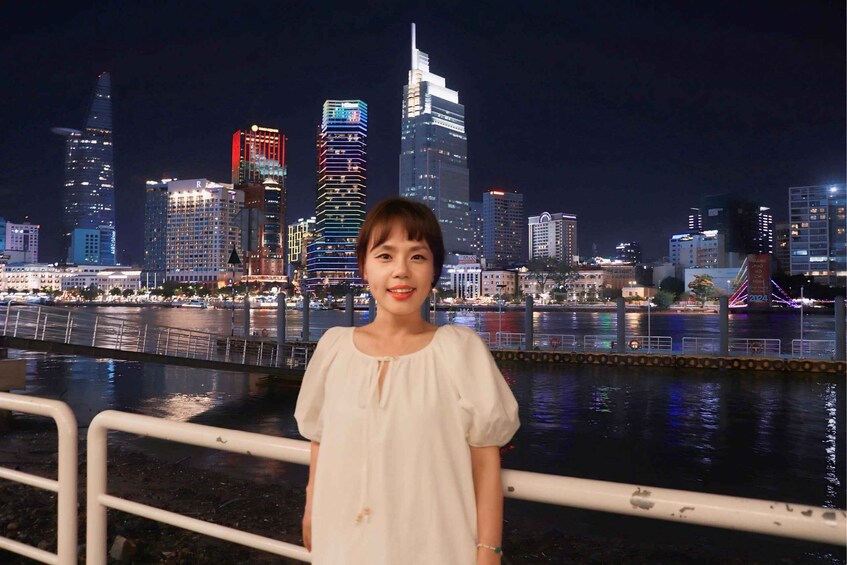 A person standing in front of a city skyline at night with illuminated buildings and a river. 5