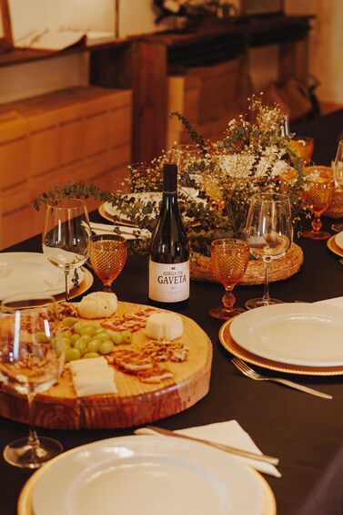 A table set for a meal with wine glasses, a bottle of wine, cheese, grapes, and a decorative centerpiece. 1