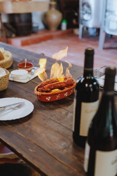 A wooden table with a basket of bread, a bowl of cheese, a bottle of wine, and a dish of sausages. 2