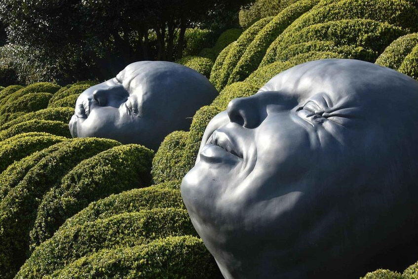 A sculpture garden with large, smooth, gray sculptures amidst neatly trimmed hedges. 1