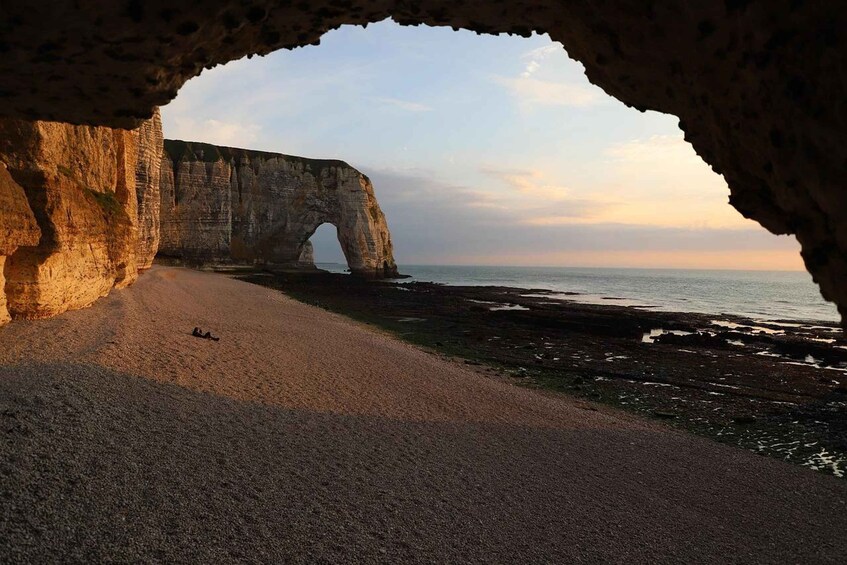 A coastal landscape with a large rock arch formation and a sandy beach. 2