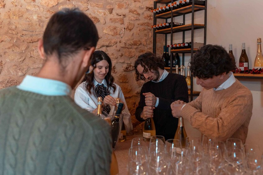 A group of people at a wine tasting event with bottles and glasses on a table. 3