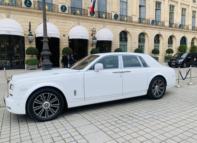 A white luxury car parked in front of a historic building with ornate balconies and a flag. 3