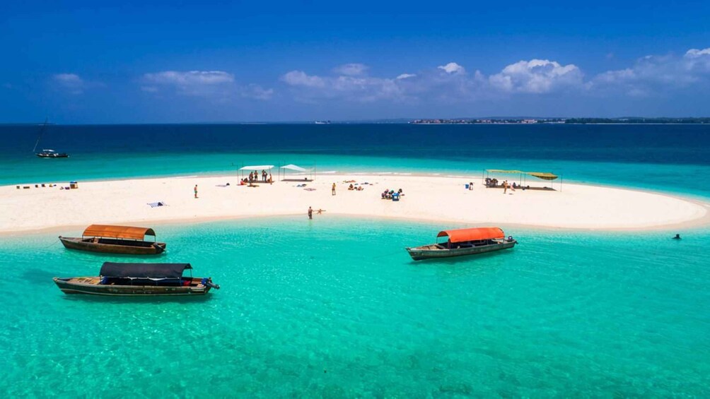 A tropical beach with clear turquoise waters, a white sand beach, and several boats anchored near the shore. 4
