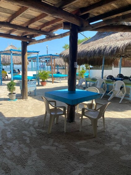 A beachside café with a thatched roof, blue table, and plastic chairs. 5