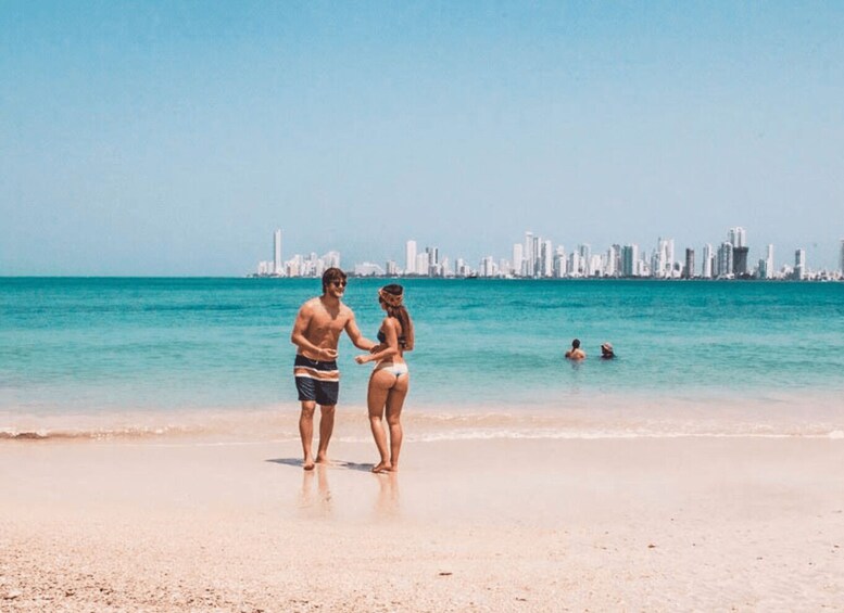 A couple standing on a beach with a city skyline in the background. 1