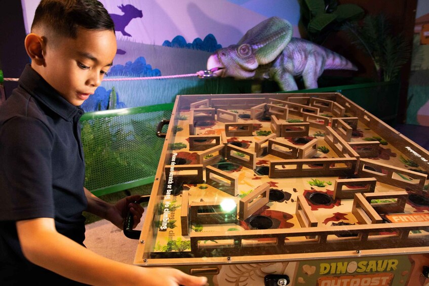 A child playing a dinosaur-themed board game with a dinosaur model in the background. 4