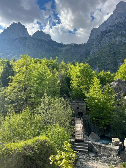 A stone bridge leading to a small stone building amidst lush greenery and mountains. 3