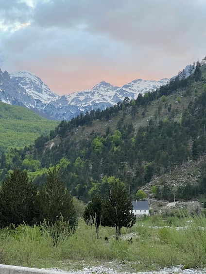 A mountainous landscape with a house in the foreground and snow-capped peaks in the background. 2