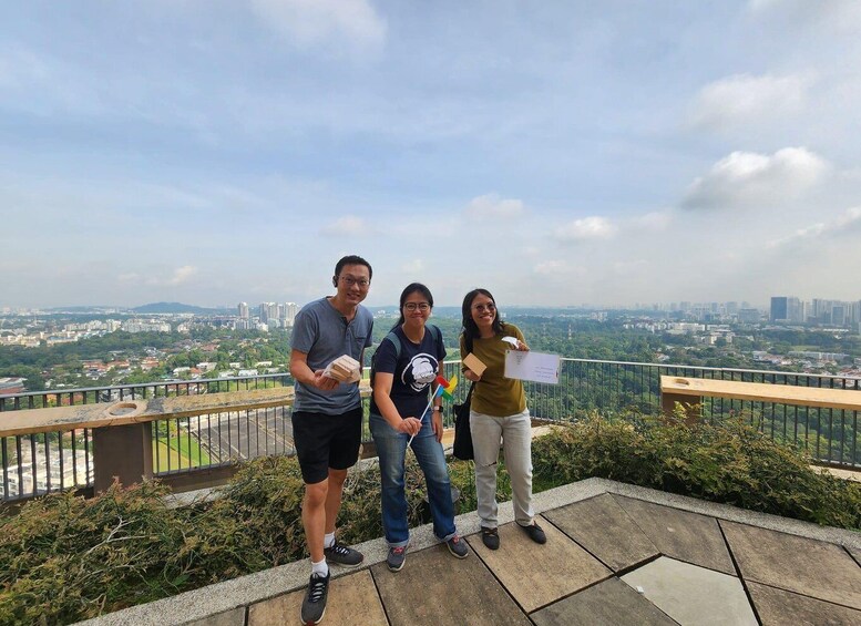 Three people on a balcony overlooking a cityscape with greenery and buildings. 1