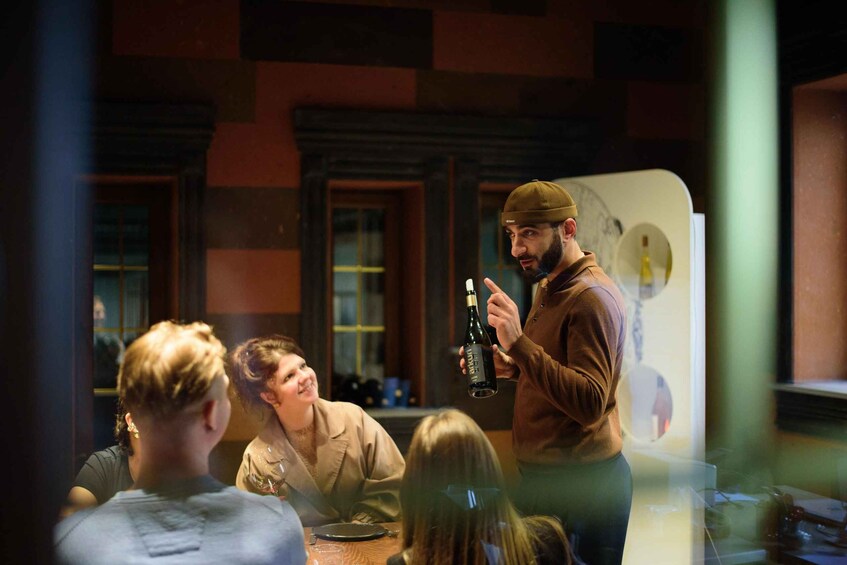 A person holding a bottle of wine in front of a group of people seated at a table. 2