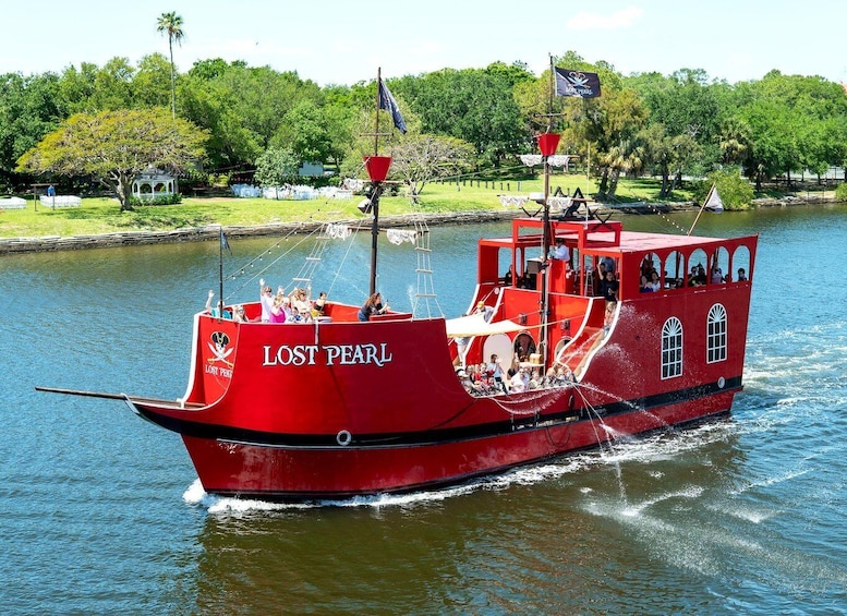 A red boat named 'Lost Pearl' on water with a dock and trees in the background. 1