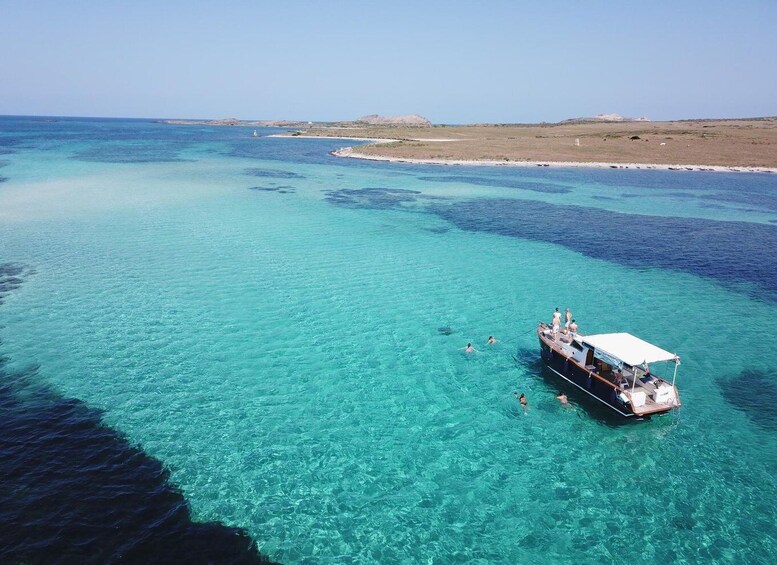 A boat with people on a clear blue sea, surrounded by shallow waters and distant land. 1
