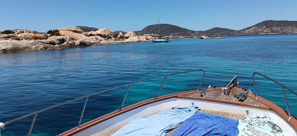 A boat on clear blue water with rocky coastline and hills in the background. 3