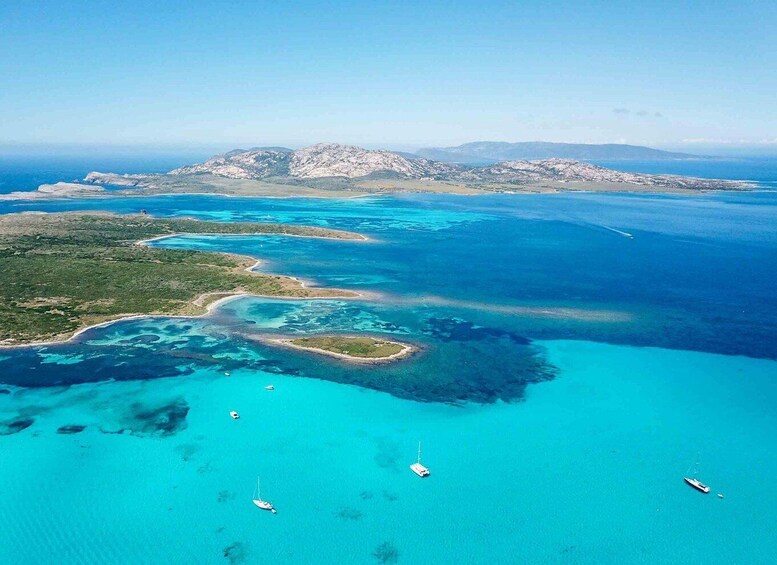 An aerial view of a coastal landscape with clear turquoise waters, a small island with a lighthouse, and distant mountains. 4