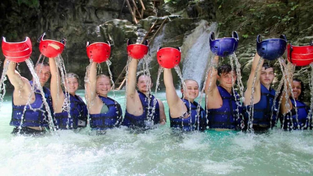A group of people in blue life jackets holding red and blue buckets over water. 1