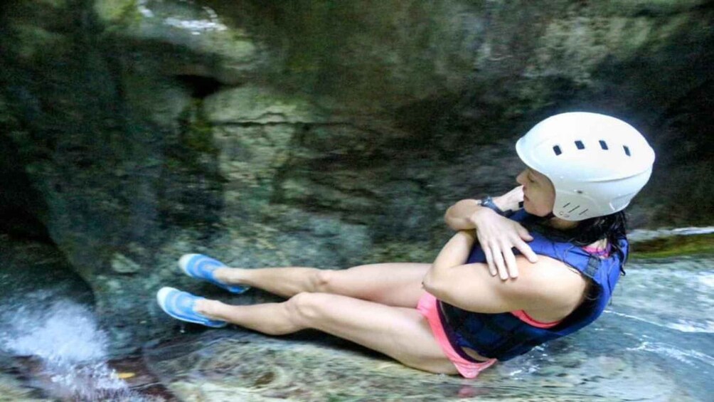 A person in a blue and pink outfit sitting on a rock with a helmet, in a rocky cave environment. 4