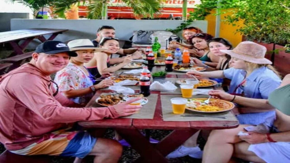 A group of people sitting at a wooden table outdoors, enjoying a meal and drinks. 5