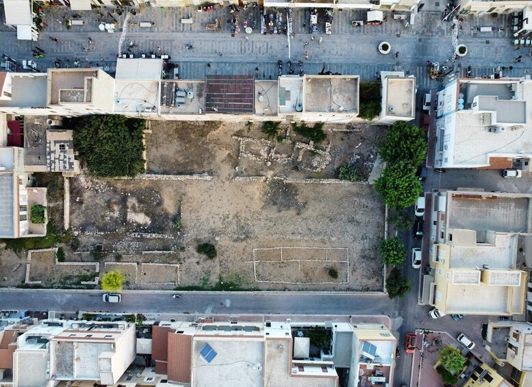 An aerial view of a city block with buildings, a central open area with ruins, and surrounding streets. 4
