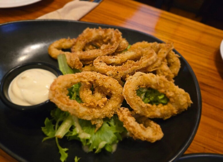 A plate of fried calamari rings with a side of dipping sauce and lettuce. 5