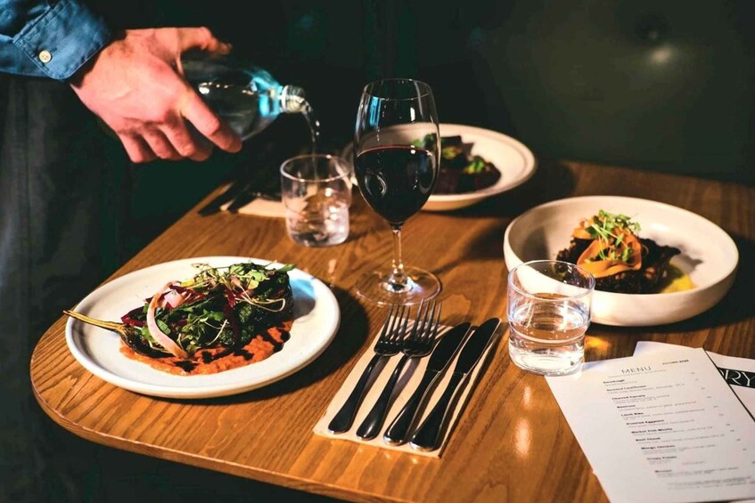 A dining table with plates of food, glasses of water and wine, cutlery, and a menu. 1