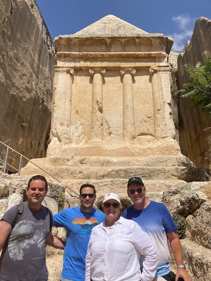 A group of people standing in front of an ancient stone structure with columns and a triangular roof. 3