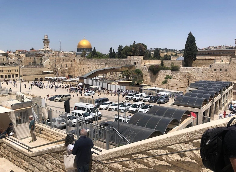 A busy parking area with vehicles, a prominent golden dome, and ancient stone walls. 1