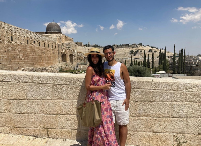 A couple standing in front of the Western Wall, with the Dome of the Rock in the background. 2