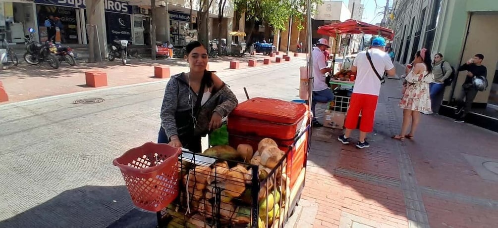 A street vendor with a cart of bread and fruits, a red basket, and a red suitcase on the sidewalk. 5