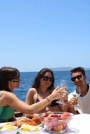 Three people toasting with wine glasses at a table with fruit and bread on a boat. 4