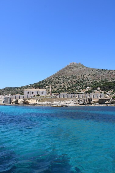 A coastal town with historic stone buildings, clear blue sea, and a hill in the background. 5