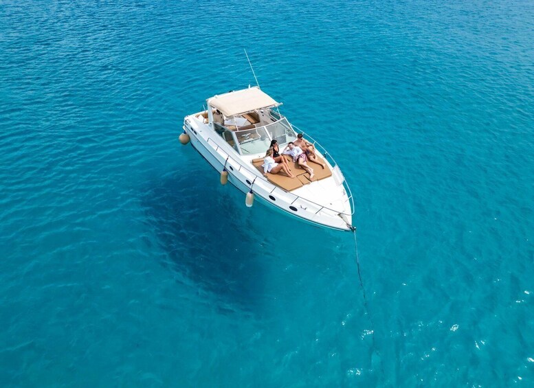 A white motorboat with a canopy, two people on deck, and clear blue water. 1