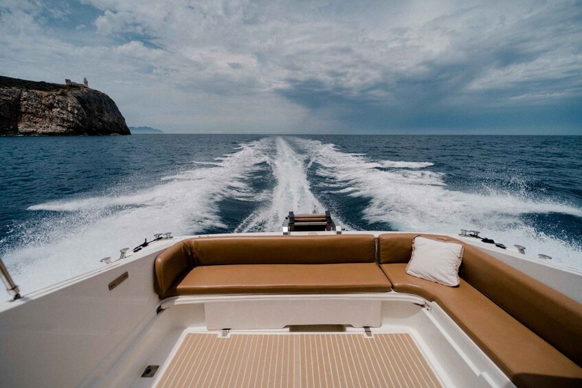 A boat's wake in the ocean, a rocky cliff, and a cloudy sky. 3