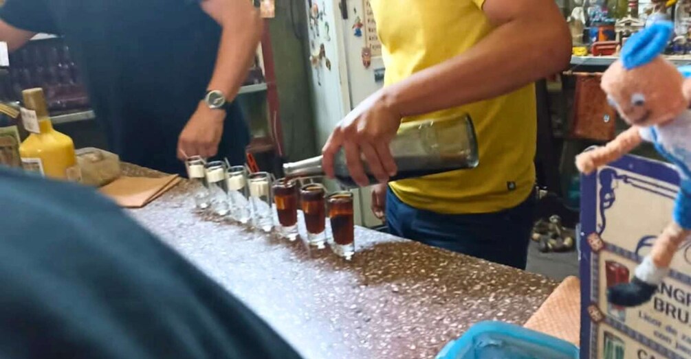 A person pouring a dark liquid into shot glasses on a bar counter. 3