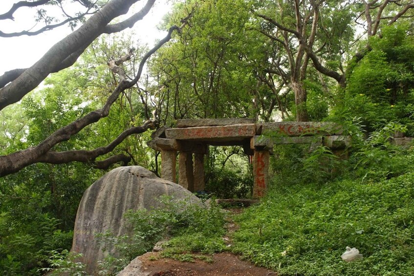 A stone structure in a forested area with a large rock nearby. 1