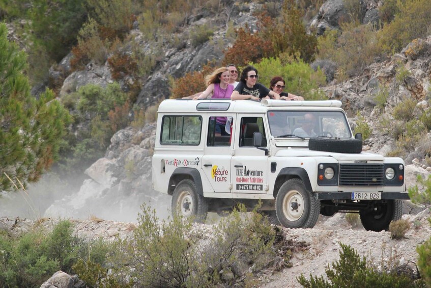 A white off-road vehicle with passengers, driving on a rocky terrain with sparse vegetation. 2