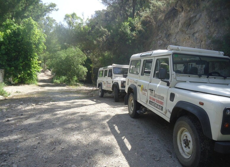 Two off-road vehicles parked on a dirt road surrounded by trees and rocky terrain. 3