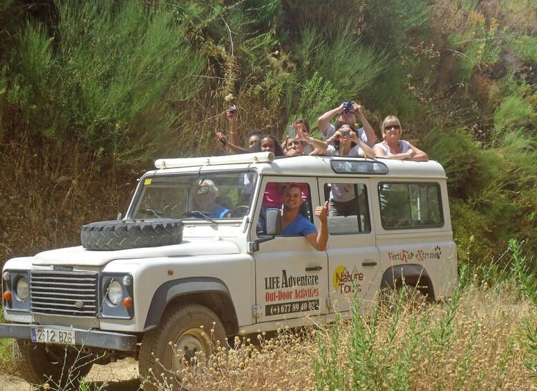 A white off-road vehicle with passengers, surrounded by dense vegetation. 1