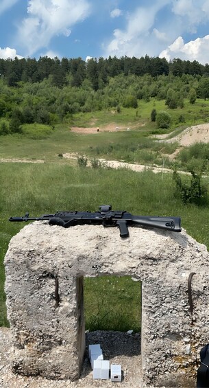 A rifle on a stone structure with a grassy field and trees in the background. 2