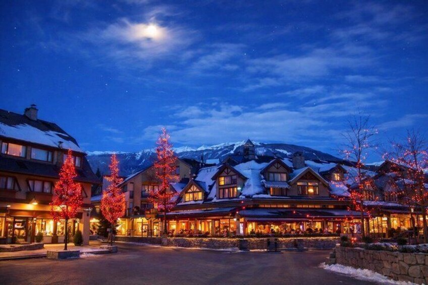 A snow-covered mountain at twilight with illuminated buildings and red-lit trees in a resort town. 4