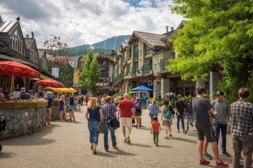 A bustling pedestrian street lined with shops and cafes, with people walking and standing. 1
