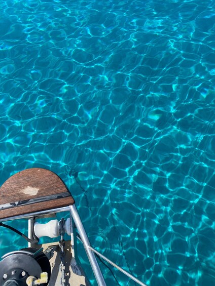 A boat's wooden deck and metal railing on clear blue water. 2