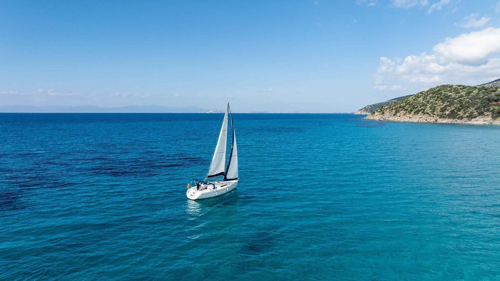 A sailboat on a calm sea with clear skies and a rocky coastline in the background. 5