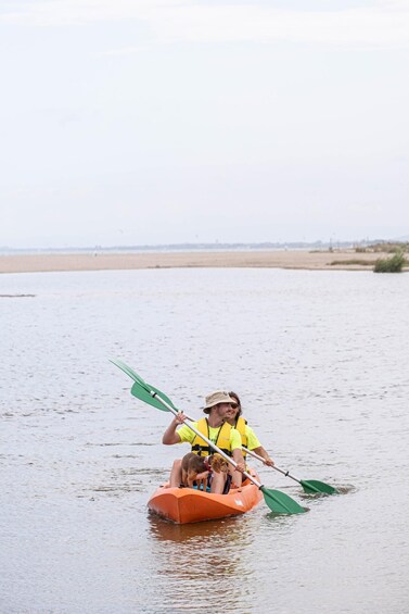 Two people in a small orange boat on a calm body of water with a sandy beach in the background. 4